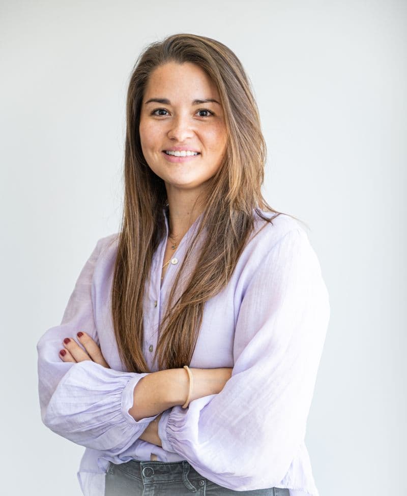 Portrait of a smiling woman with arms crossed, wearing a lavender shirt
