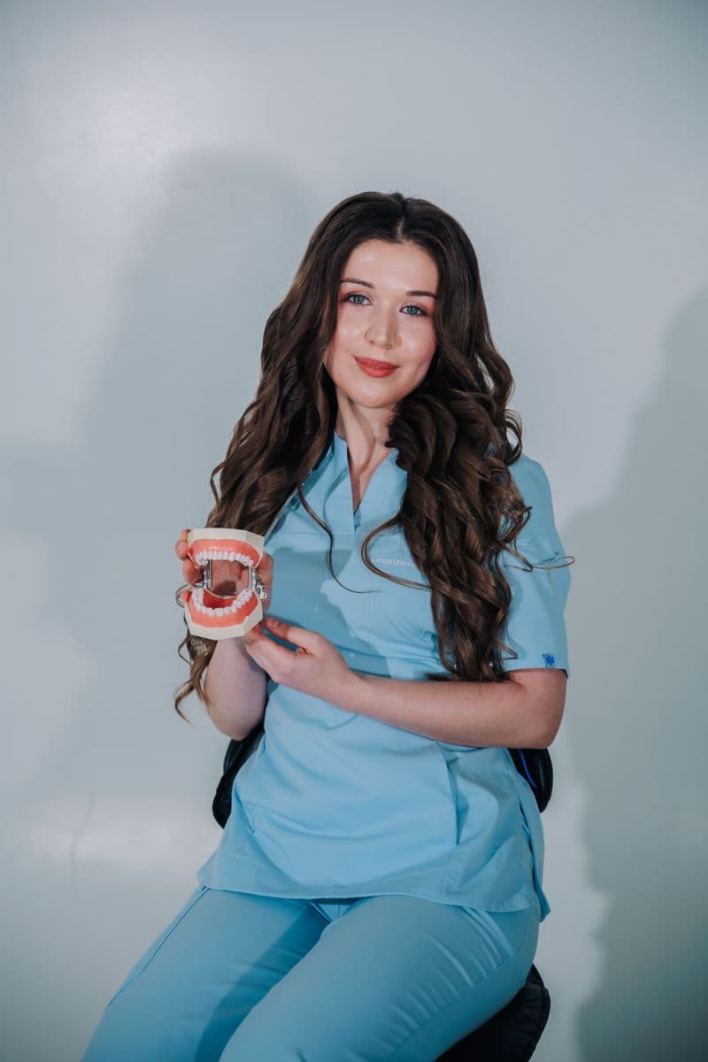 Portrait of Jordan Ellis, RDA, a smiling female orthodontic assistant holding a braces model