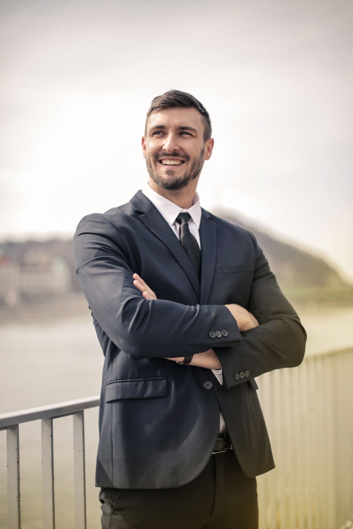 An adult man in a suit smiling confidently outdoors