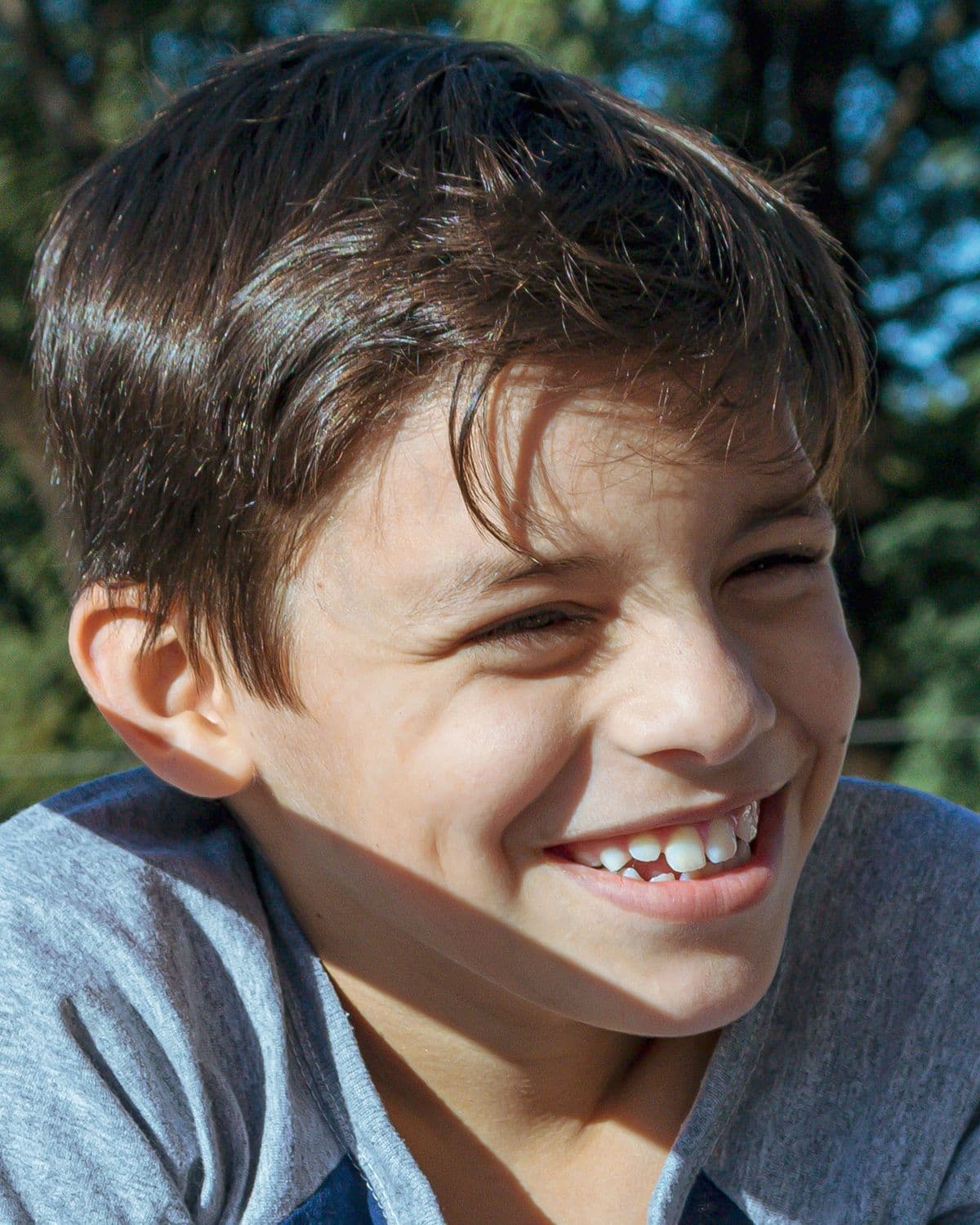 A happy young boy smiling outdoors, showing a gap tooth grin
